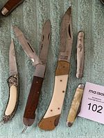 Photo of six custom cut knives in various styles and materials on a green carpet background.
