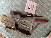 Overview of various fishing tool cutters and knives laid out on a light blue textured fabric.