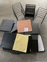 Top-down view showing three black metal desk organizers and seven assorted binders including one in peach color and several in black, some open revealing pages and tabs.