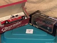Photo showing two die-cast collectible model cars in their boxes, one a red and white Mac Tools Cheerwine Softdrink racing pickup, the other a maroon Maisto Mercedes Benz 500SL convertible.