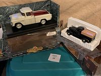 Die-cast models in packaging: cream and maroon Chevy 3100 Cameo 1:18 scale in branded box, and black 1940 Ford pickup truck bank 1:64 scale in plastic packaging