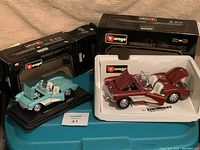 Two die-cast model cars in original boxes, one turquoise and one maroon 1957 Chevrolet Corvettes by Bburago.