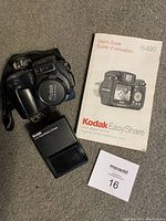 Kodak EasyShare DX6490 camera body with flip-out LCD screen, user manual, and maxsold lot number card.