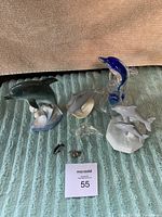 Photo showing five dolphin figurines including a blue glass dolphin, ceramic dolphin music box, and others on blue fabric background