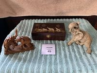 View of the entire lot on blue textile: wooden jewelry box with elephant carvings on lid center, hand-carved teak elephant pair on left, gray ceramic elephant on right.
