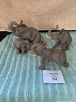 Four Andrea by Sadek porcelain elephants grouped together on a teal textured blanket, showing varying sizes and poses.