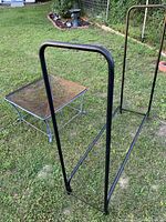 Large rectangular metal frame fire log holder, black painted, simple tubular construction with rounded vertical supports and a horizontal base bar.