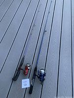 Two fishing rod and reel combos laid on wooden surface showing both rods and attached reels in full length.