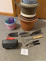 Photo showing the garden pots stacked and various gardening tools including trowel, pruning shears, scissors, hand cultivator and plastic seed starter box