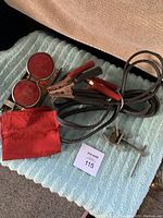 Overview of jumper cables with red and black clamps, round metal reflectors with red lenses, and red help flag on cloth surface.