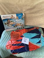 Photo of colorful surfboard-shaped striped inflatable pool float laid flat on a surface with a blanket background, showing no visible damage or holes.