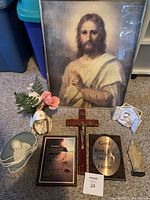 Photo displaying framed Jesus portrait, crucifix, God Bless plaque, Mother Mary statue with flowers, devotional plate, Footprints poem, praying hands statue, and nativity figurine.