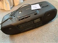 Front view of black Sony portable audio device showing speaker grilles and control panel with tuning dial, radio display, and cassette door.