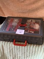 Closed plastic toolbox with transparent lid showing organized compartments of screws, nails, and hardware fittings.