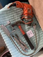 Electric drill, hammer, vise grips, and BBQ light shown together on towel