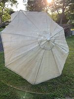 Photo of used beige outdoor umbrella open on grass, showing fabric faded with sun shining in background