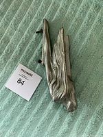 Side view of the hood ornament showing elongated form and mounting screws.