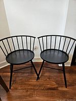 Two black wooden low back Windsor dining chairs side by side showing overall design and condition.