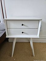 Front view of white nightstand showing two drawers and legs
