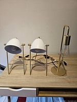 Photo showing two Fila table lamps with white cone-shaped shades and brass-tone wire frames beside one gold-tone Structube Rimini lamp