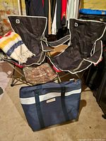 View of two outbound camping chairs with black fabric and white trim, HBC style blanket with colorful stripes draped over one chair, blue Keepcool cooler bag in front on floor.