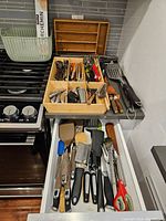 Two wooden segmented utensil storage trays with organized kitchen and BBQ utensils placed on stovetop and countertop.