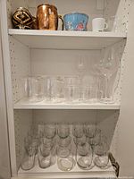 Photo showing various sizes of clear drinking glasses on shelves, including tall glasses and stemmed wine glasses