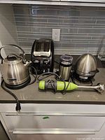 Kitchen counter with all five appliances: KitchenAid kettle, T-fal Avante toaster, KitchenAid hand blender, coffee grinder, and Cuisinart egg cooker pictured together.