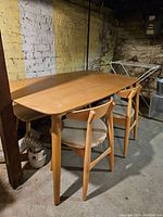 Photo showing wooden dining table with rounded edges and tapered legs with two chairs underneath, set in basement environment.