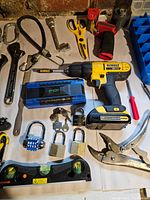 Close-up of DeWalt cordless drill with battery attached, charger, hand tools and padlocks