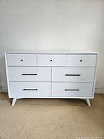 Front view of white dresser with three small top drawers and four larger bottom drawers on tapered legs.