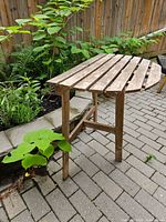 Side view of weathered wooden side table showing slatted top and leg structure near garden area on stone pavement.