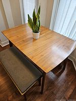 Angled view of table top and one bench showing wood grain and grey upholstered seat