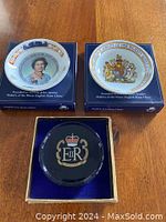 Front view of two commemorative plates and one glass paperweight in display boxes.