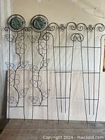 Four metal garden trellis standing upright, showing two with leaf and flower design and two with scroll designs