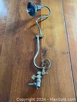 Full view of the antique brass gas fitting showing the curved pipe with scroll design and valve mechanism.