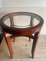 Photo showing top view of round glass surface inset in wooden frame of the table. Wood finish is dark brown with decorative engraved lines visible on legs.