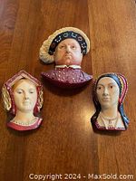 Three head plaques on wooden table: male center, two females flanking