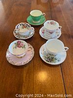 Overview of 5 cups and saucers with varying floral and color designs displayed on wooden table