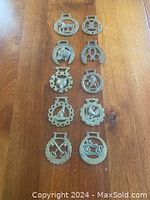All ten vintage metal horse brasses arranged in rows on wood surface showing various horse and horseshoe designs.
