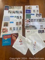 Photo showing two sheets of commemorative 1st Day Covers and postmarked envelopes related to British royal events plus two embroidered napkins and a small red booklet.