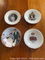 Four small commemorative plates arranged on wooden table showing fronts with royal family portraits, insignia, and commemorative themes.