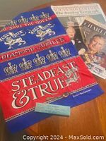 Colorful commemorative towel for Queen Elizabeth's Silver Jubilee and Diamond Jubilee with royal motifs and inscriptions lying flat on wood surface along with souvenir papers related to Charles' coronation.