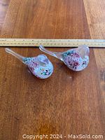 Photo of two solid glass bird figurines on a wooden surface with ruler for scale showing colors and size.