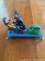 Front view of mechanical dentist bank showing patient and dentist with the patient in the dental chair and coin slot on the base.