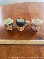 Three mini Toby character jugs on a wooden table with a ruler for scale