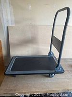 Side view of a black platform cart with gray handle against a plain background