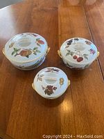 Set of three Royal Worcester Evesham ceramic covered bowls of different sizes shown together on a wood table.