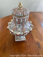 Full view of porcelain urn with lid on wooden table showcasing gadrooned body and floral panels.
