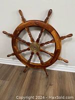 Full front view of 36" hardwood ship wheel leaning against wall